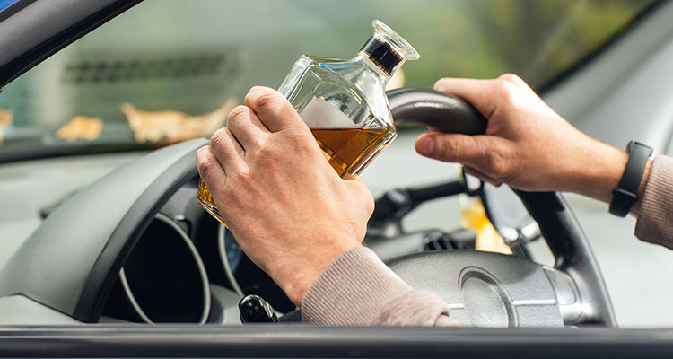 Driver behind the wheel holding a bottle of alcohol, illustrating the drunk driving crashes that give rise to Minnesota dram shop liability.