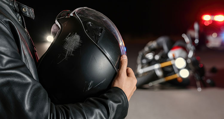 Man holding a motorcycle helmet near a crash scene, representing injured riders who need a Minneapolis motorcycle accident lawyer.