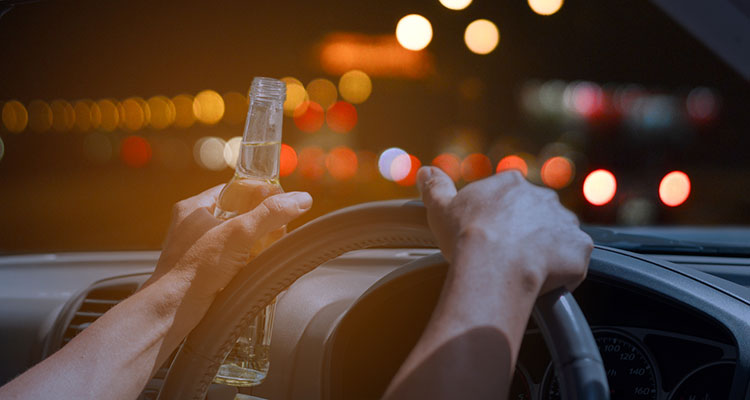 Driver holding a bottle of alcohol behind the wheel, illustrating the danger of holiday drunk driving accidents in Minnesota.