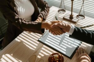 Lawyer and client shaking hands over legal documents in an office, symbolizing agreement, settlement, or successful legal consultation.