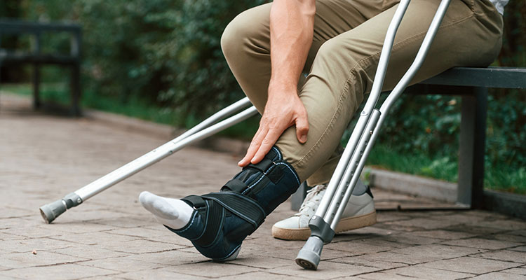 Man using crutches outdoors while holding an injured leg, illustrating recovery and long-term impact considered when deciding whether to accept a settlement or take a personal injury case to trial.